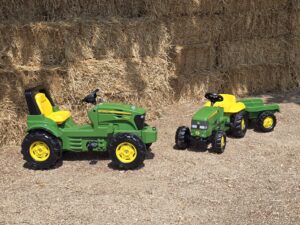 two children's ride on tractors are show in front of some straw bales