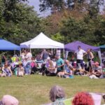 a crowd of people at an event. gazebos are seen in the background