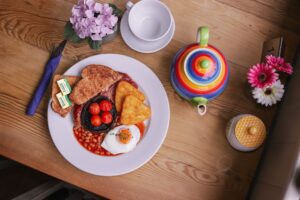 a full english breakfast is shown on a table with a colourful tea pot next to it